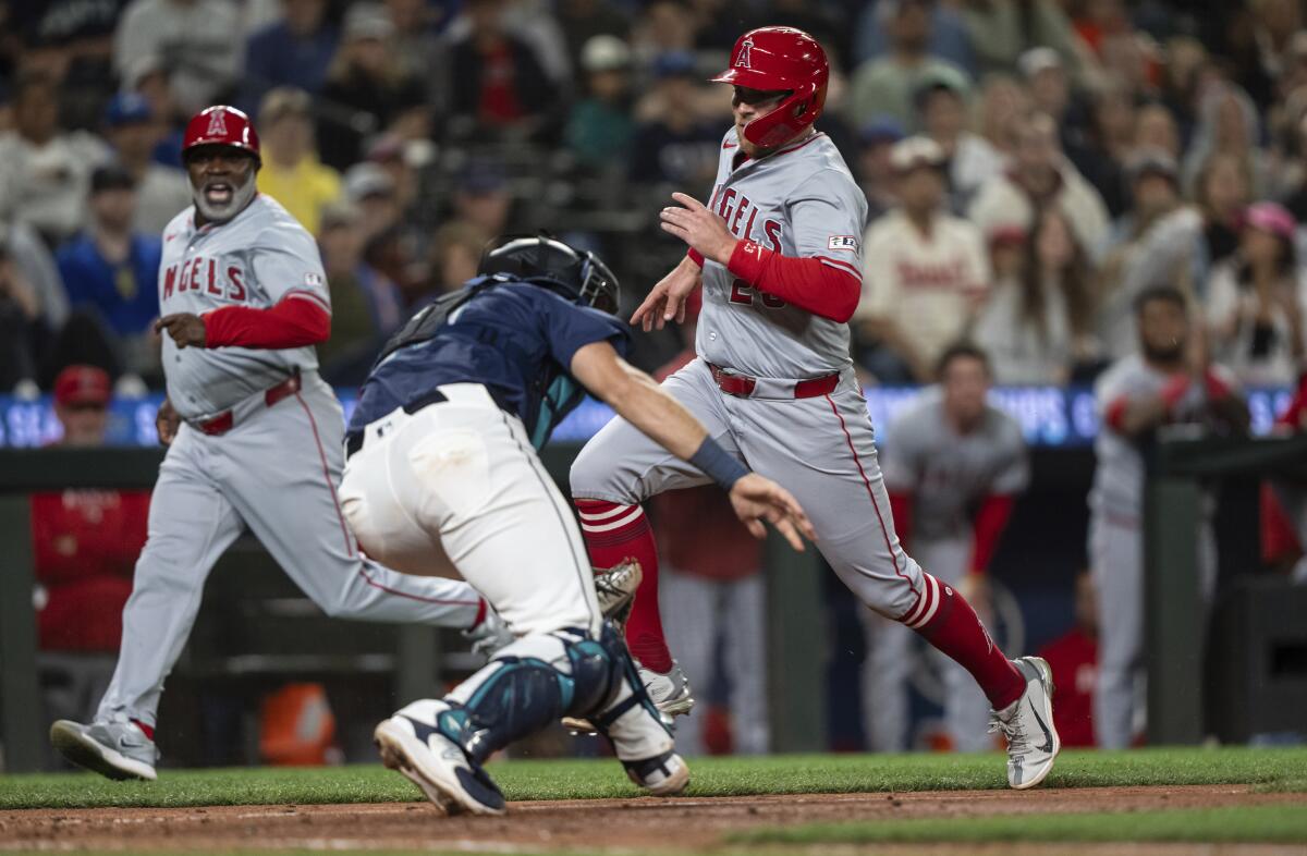 Los Angeles Angels' Brandon Drury, right, runs past Seattle Mariners catcher Cal Raleigh.