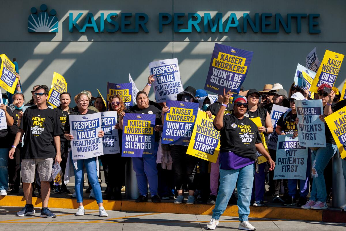 A crowd holding picket signs outside a building with a sign that says Kaiser Permanente 