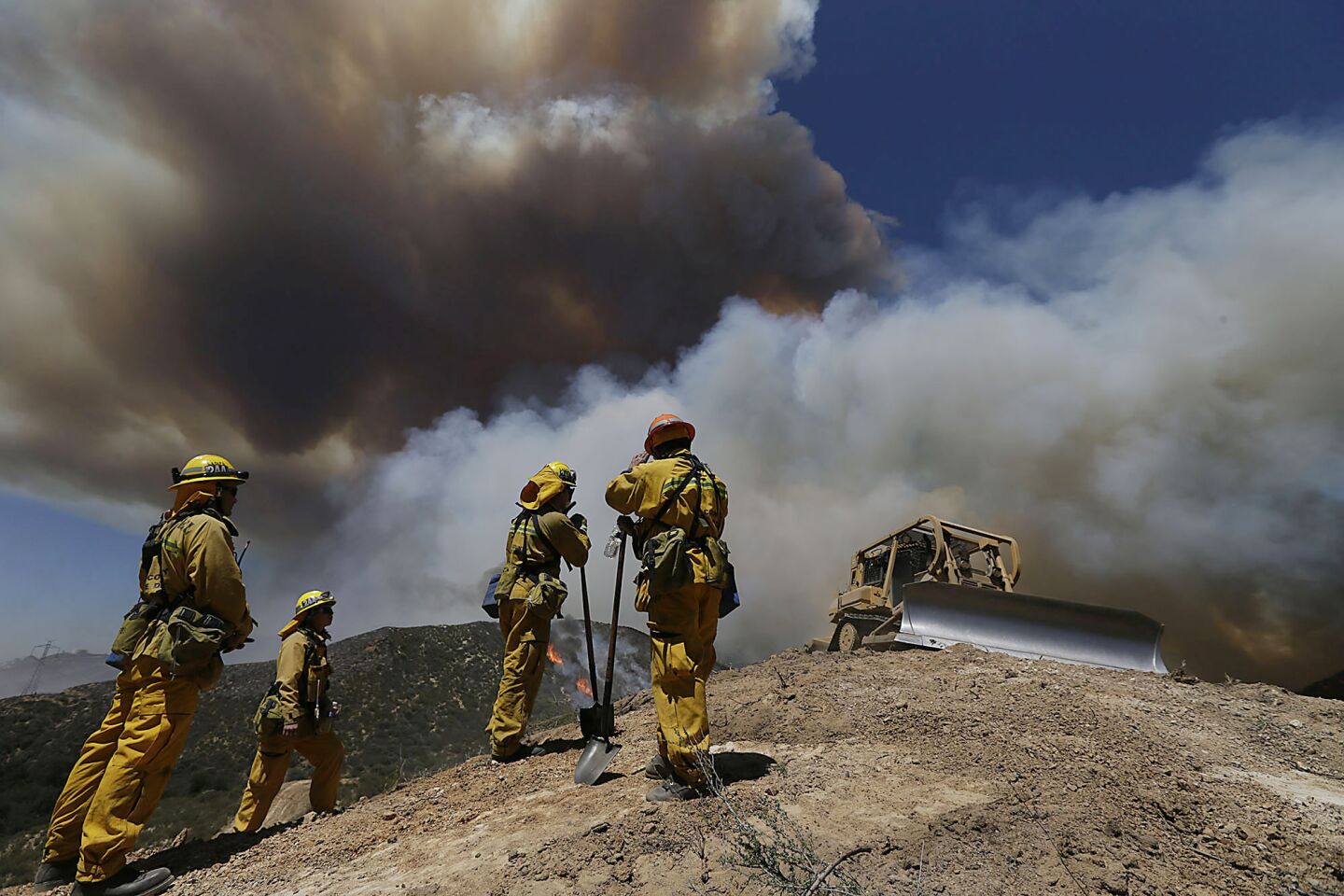 A crew from Duarte stands by as a bulldozer cuts a fire line in an effort to slow the progress of the Powerhouse fire near Castaic.