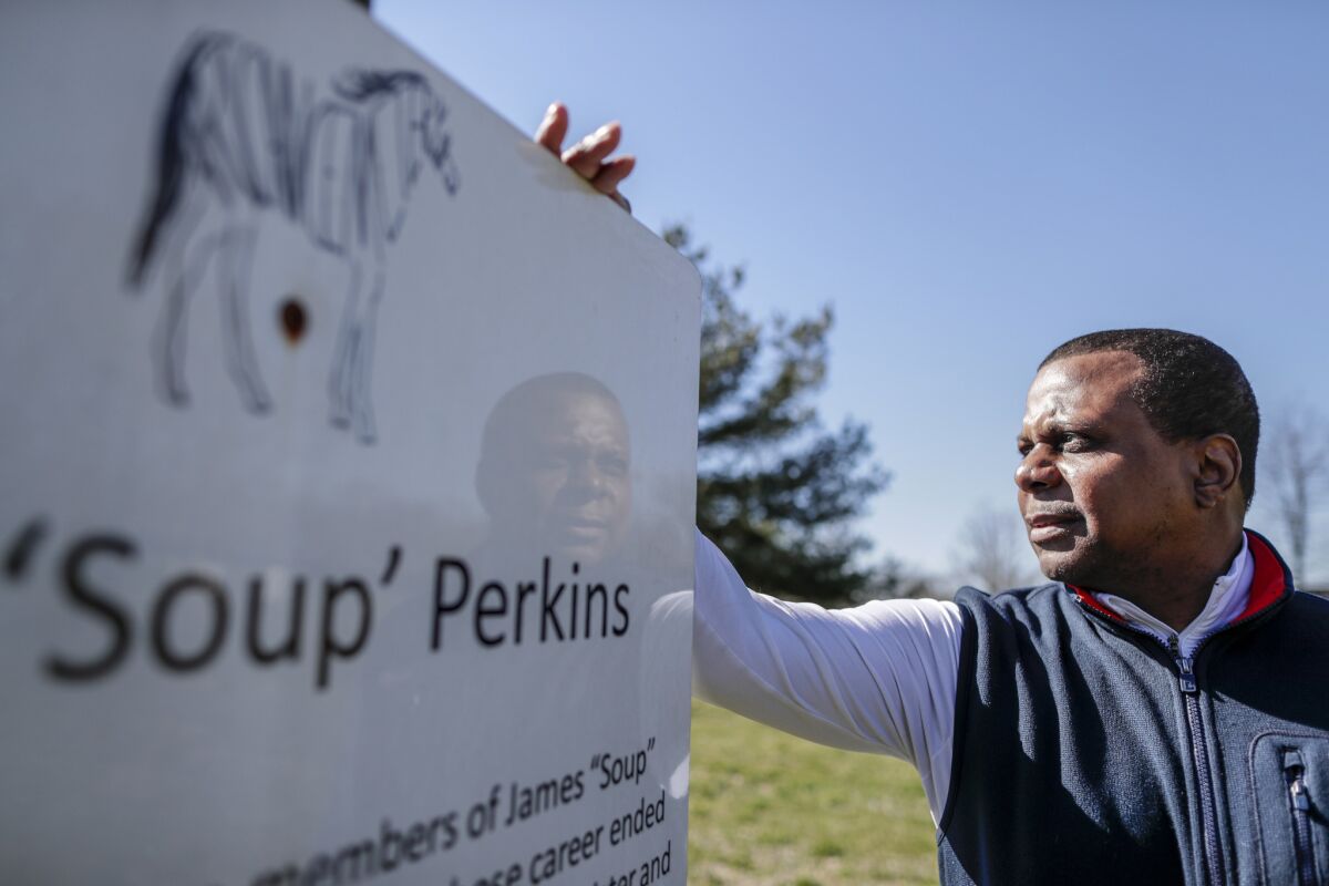 Leon Nichols stands next to a sign honoring James “Soup” Perkins at African Cemetery No. 2. (Robert Gauthier / Los Angeles Times)