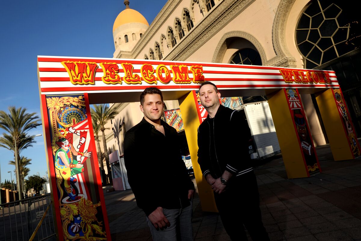 Two men in front of a carnval "welcome" sign