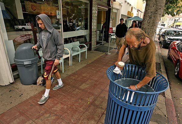 A man digging through a trash can in Westwood Village last week. Because of a new improvement district, litter is getting picked up, tree branches are decked with lights and chewing gum is being scrubbed off walkways.