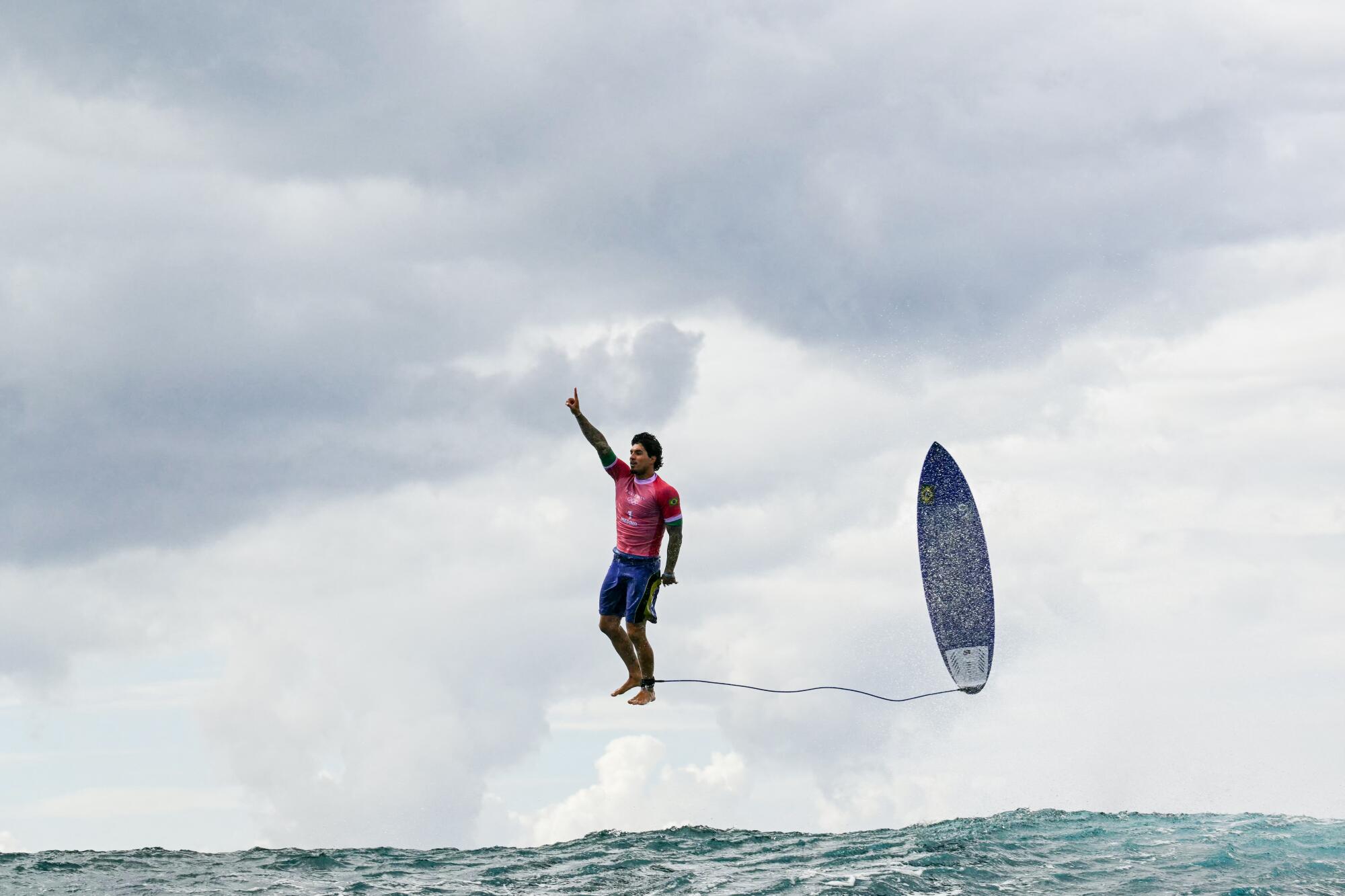 Brazil's Gabriel Medina holds up one finger while in midair, upright and parallel to his surfboard, over the ocean