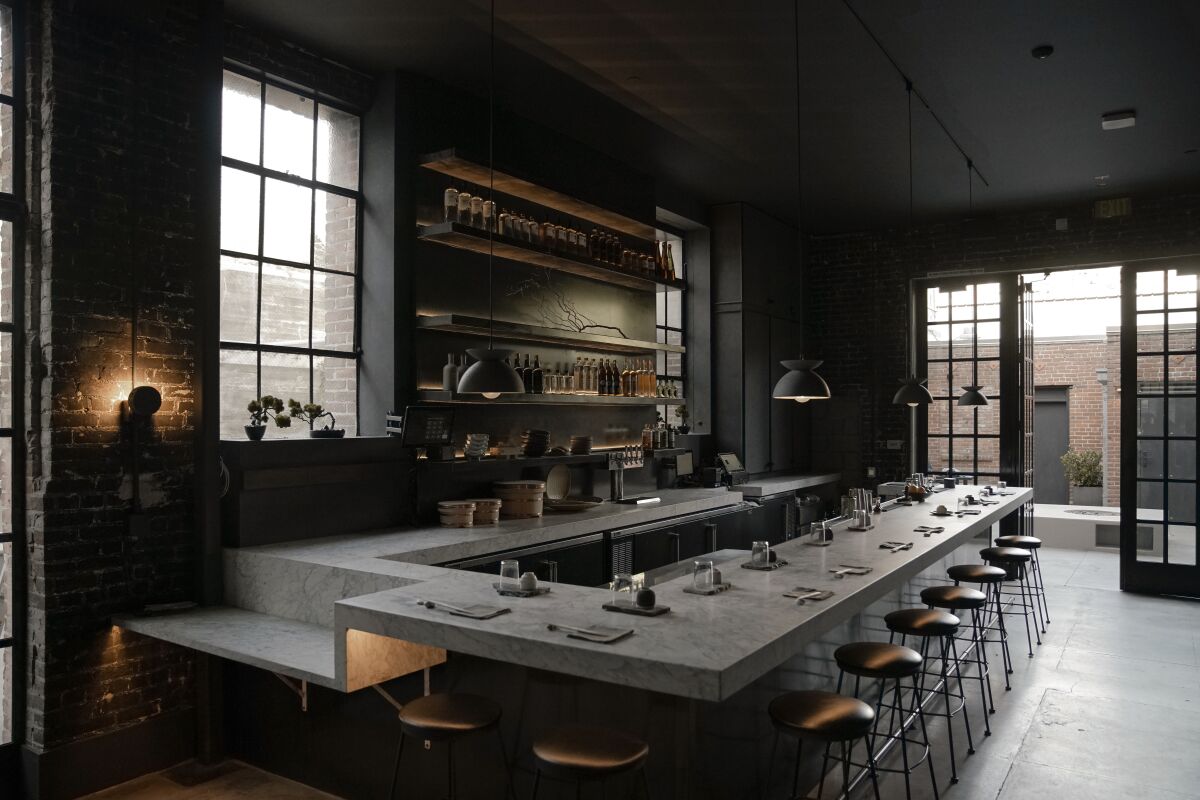 A moody photo of the minimalist sushi bar at Kodo, which features open shelving and a marble sushi bar.