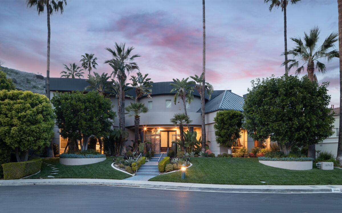 A short walkway leads from the street up to a one-story home with glass doors at twilight