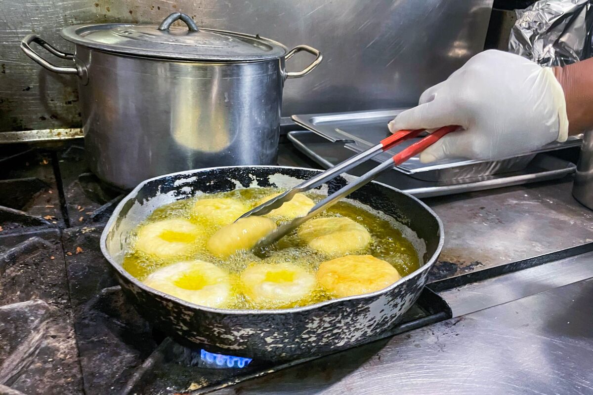 A hand holding tongs over a pan of dumplings frying in oil.