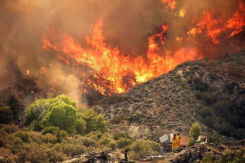 Two firefighters keep an eye on the Sawtooth fire burning in a canyon in Morongo Valley Friday afternoon.
