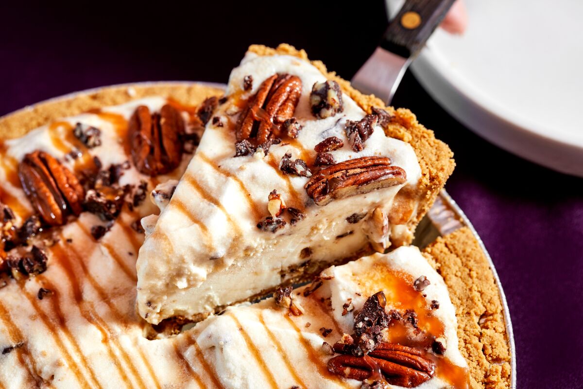 A piece of Dear Bella Creamery's pecan-covered turtle cheesecake ice cream pie is scooped out of the rest of the tin.
