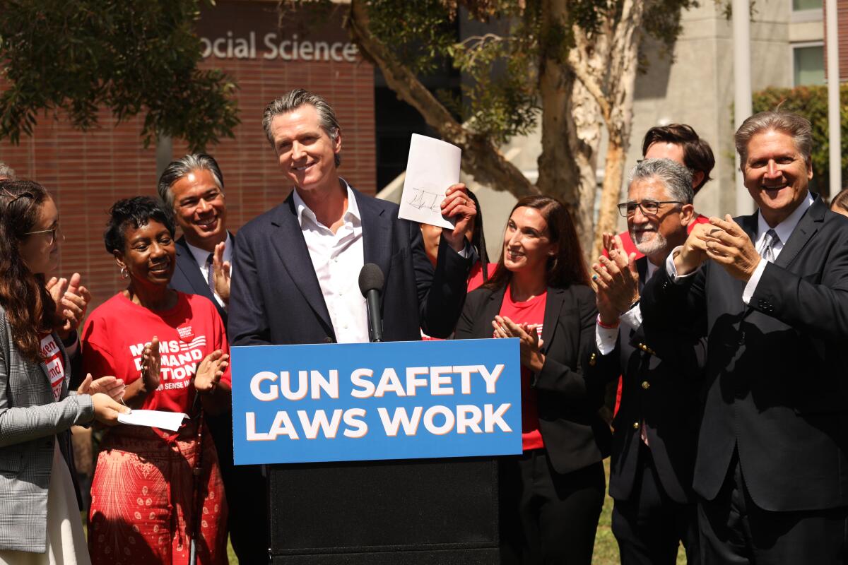 Newsom holds up a piece of paper with his signature at a lectern with a sign reading Gun Safety Laws Work