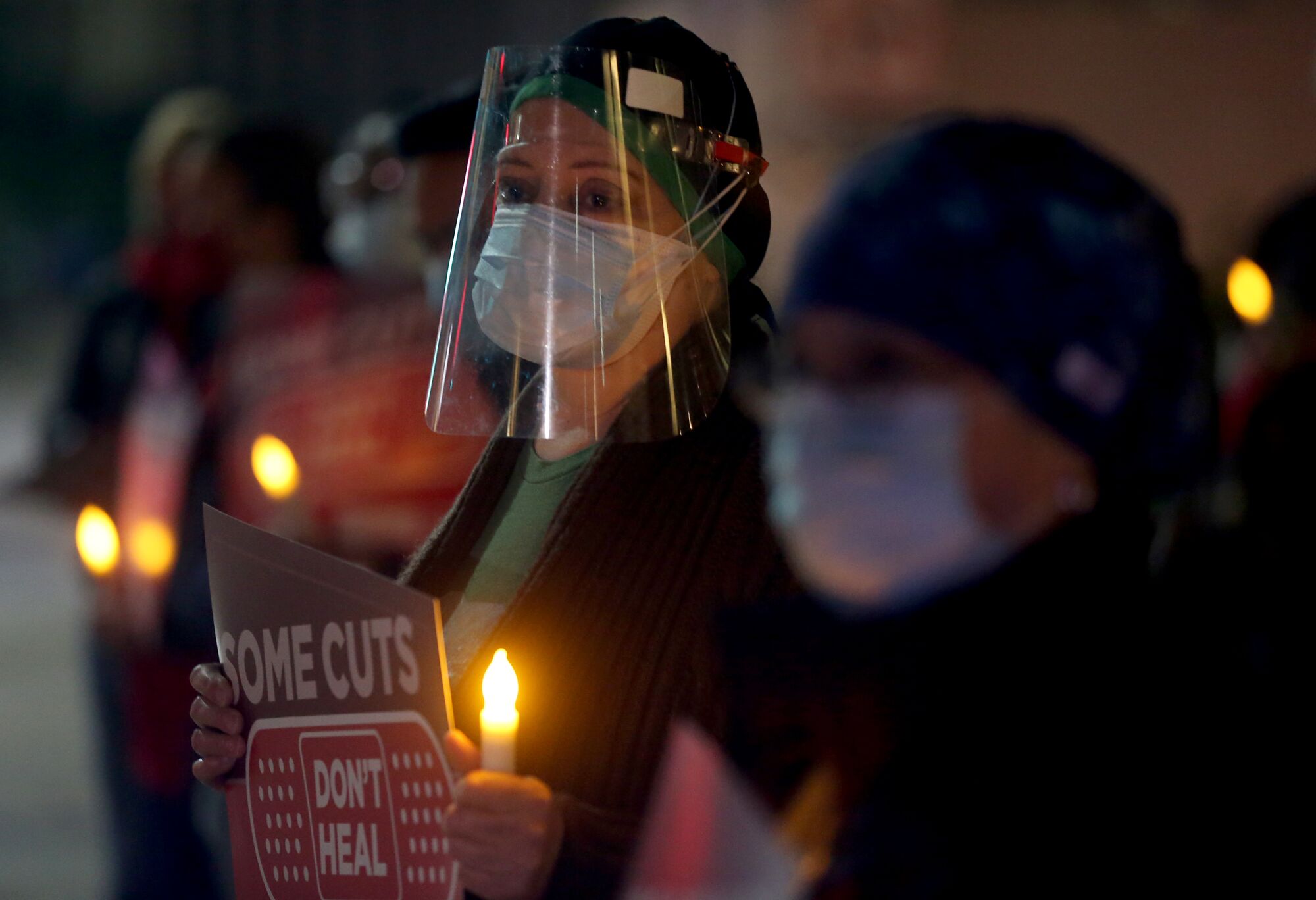Nurses hold battery operated candles; one carries a sign that reads "Some cuts don't heal."