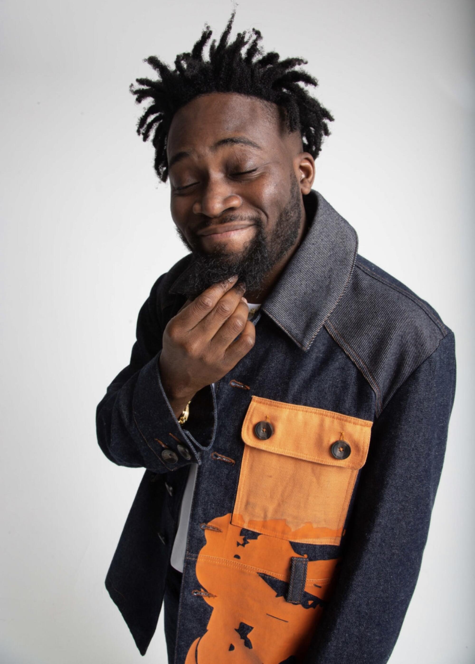 A man strokes his beard while wearing a denim jacket