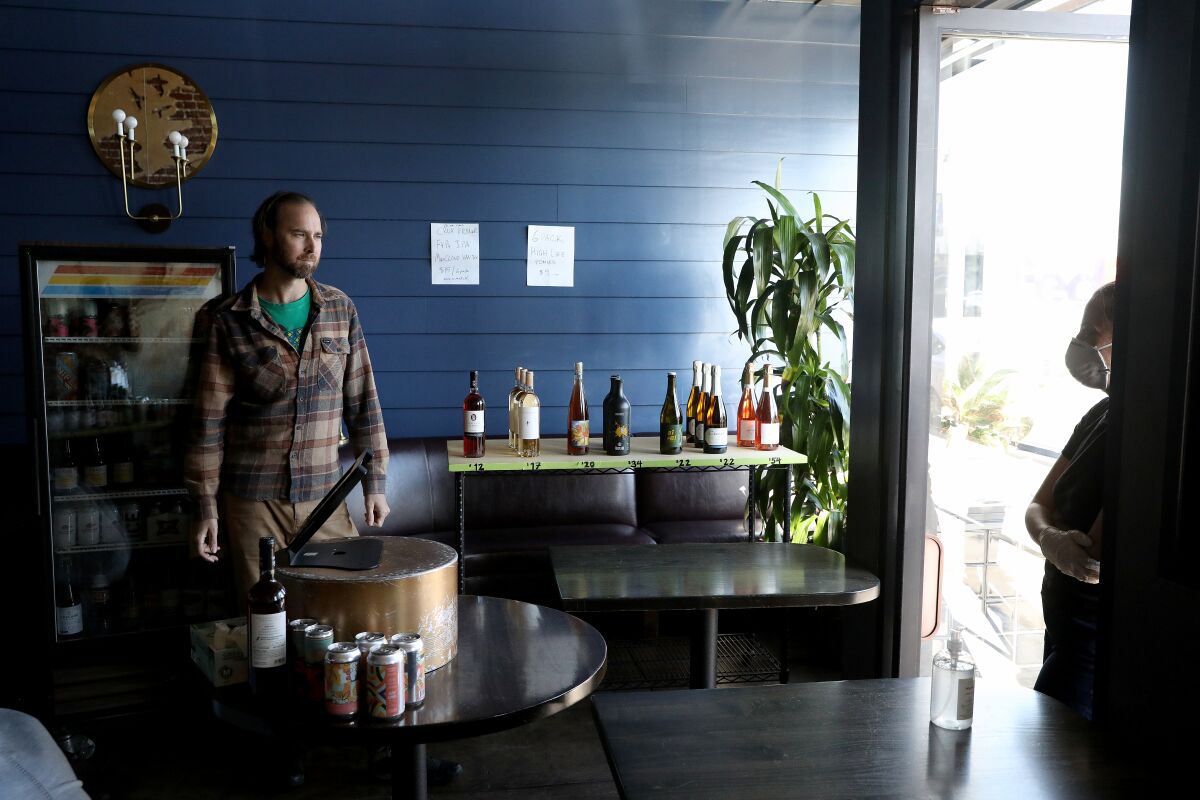 Owner Zach Negin, left, speaks with customer Marina Olshanski while she purchases wine and other alcoholic beverages to-go at Tabula Rasa bar in L.A.'s Thai Town.