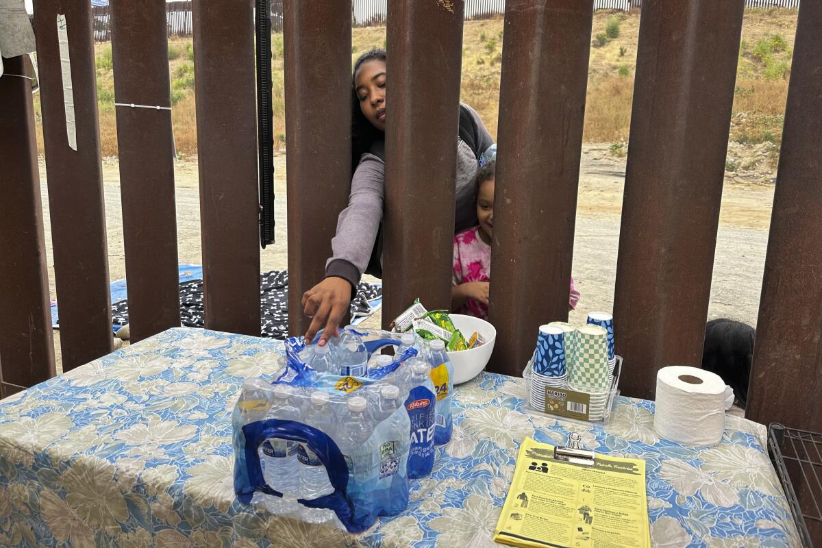 A woman reaches through a fence toward bottles of water.