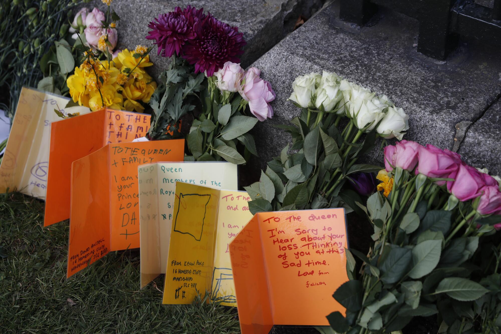 Cards written by children as a tribute to Prince Philip stand on grass amid cut flowers outside Windsor Castle
