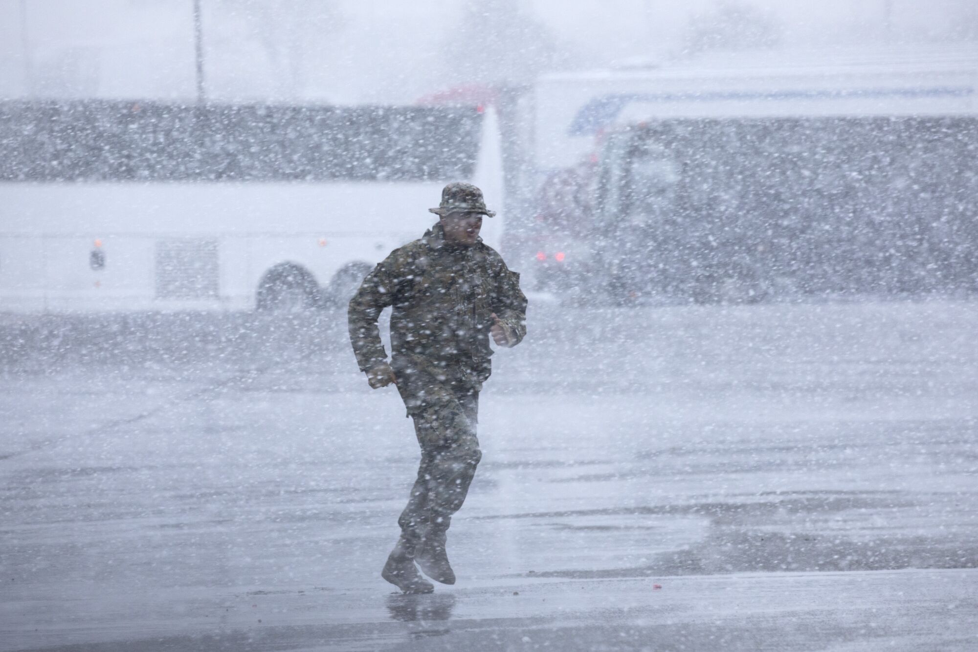 A man in camouflage clothing runs across a slushy parking lot as snow falls