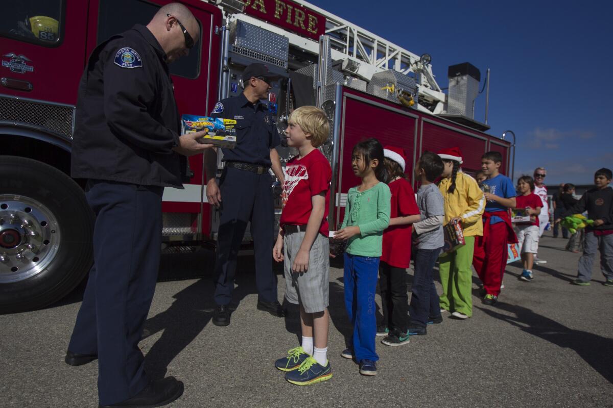 Costa Mesa Firefighter Ken McCart left, and Engineer Anthony Mancillas take a gift from Kaiser Elementary School student Breden Hayward, 8, for the Costa Mesa Fire Department's charity Spark of Love on Friday, December 20. (Scott Smeltzer, Daily Pilot)