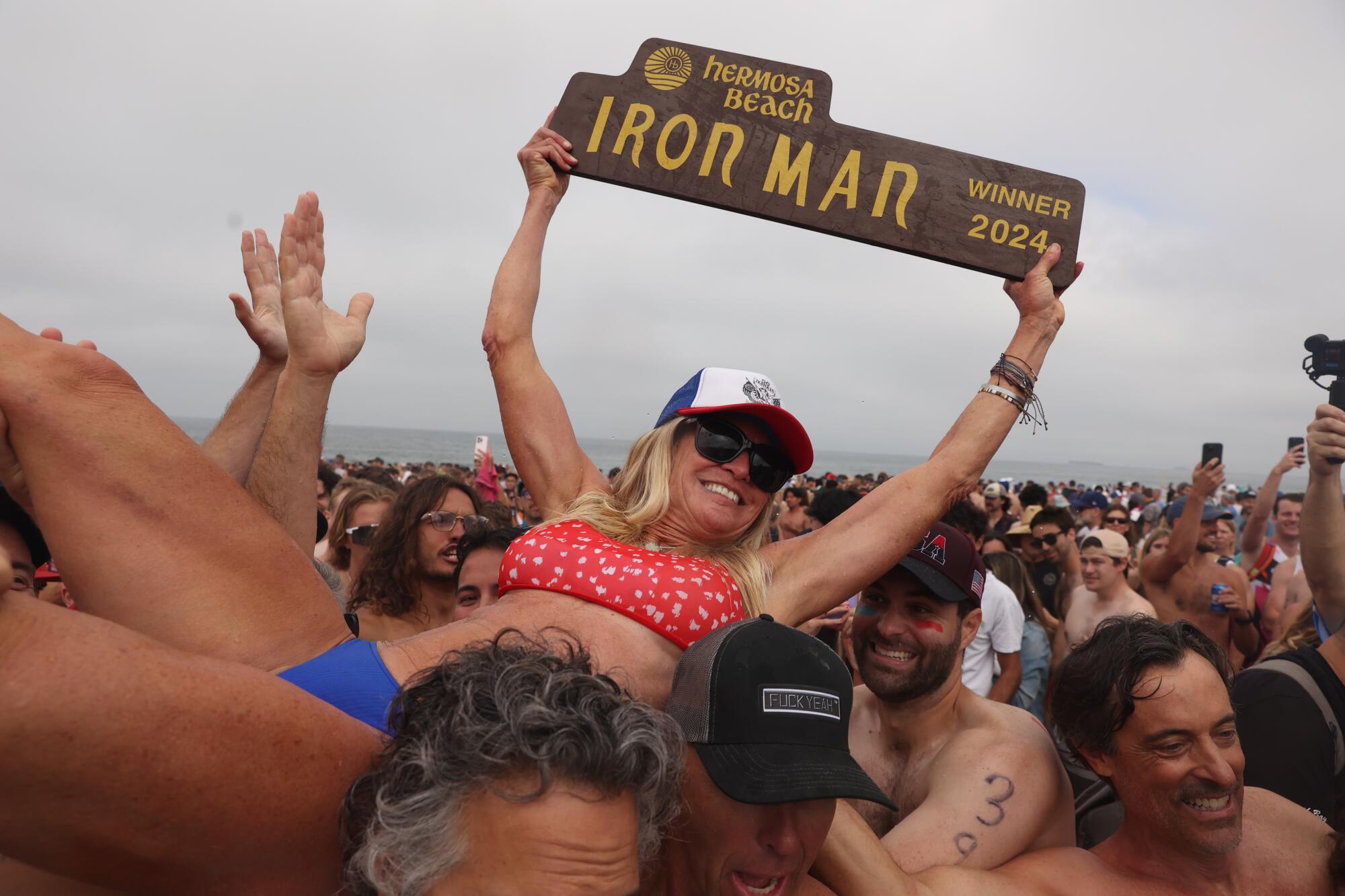 A woman holds a sign that reads "Iron Man" as she is lifted into the air by many people.