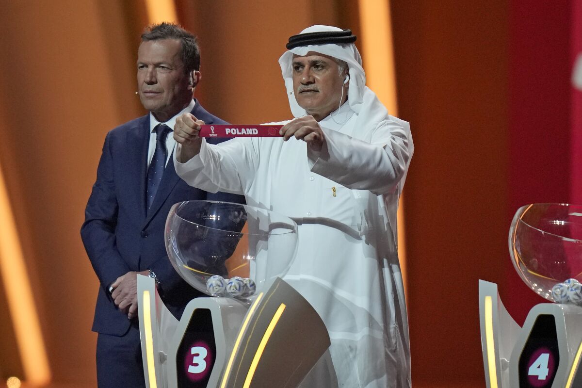 Former Qatari soccer international Adel Ahmed MalAllah holds up the name of Poland as he assists in the 2022 soccer World Cup draw at the Doha Exhibition and Convention Center in Doha, Qatar, Friday, April 1, 2022. (AP Photo/Darko Bandic)