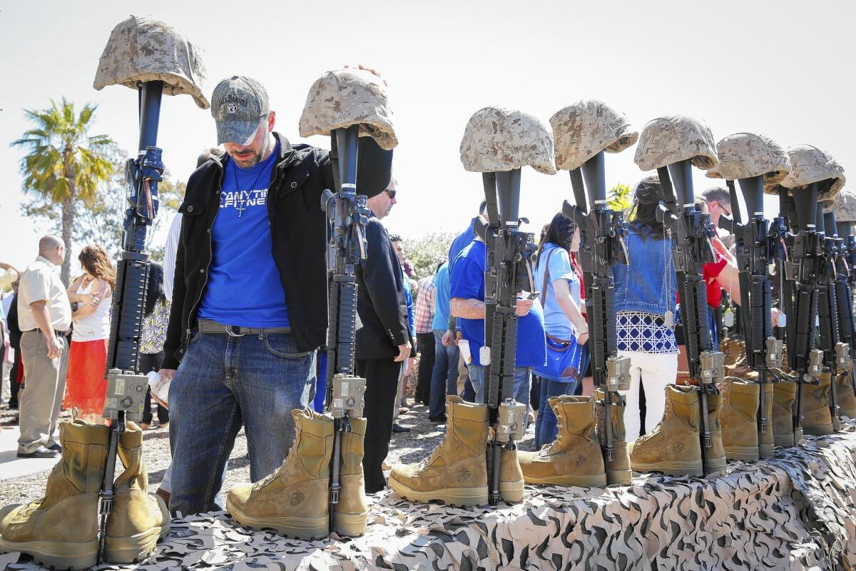 Retired Marine Justin Neumeier places his hand on a helmet while remembering his friends killed in battle in Ramadi, Iraq, during a memorial for its 10th anniversary at Camp Pendleton.