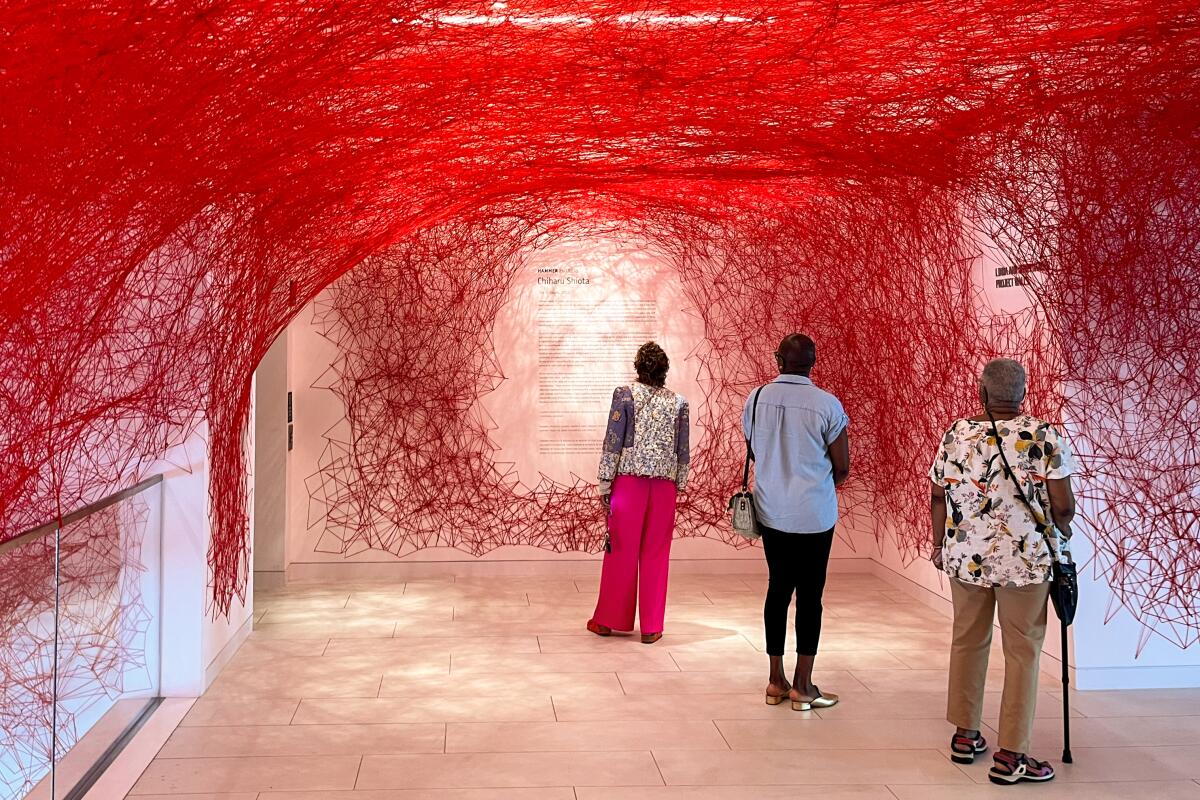 A photo of the interior of the Hammer Museum at UCLA with a red, web-like structure on the ceiling and walls. 