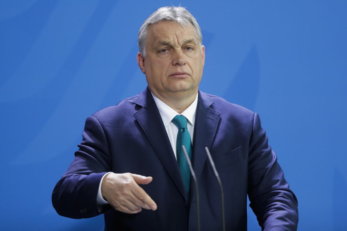 Hungary's Prime Minister Victor Orban stands in a suit at microphones.