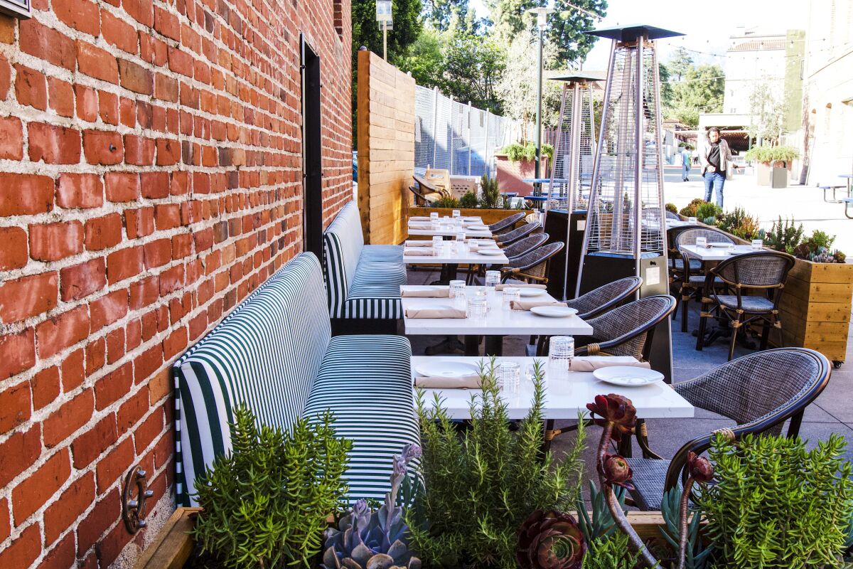Photo of a restaurant patio featuring greenery and striped banquette seating.