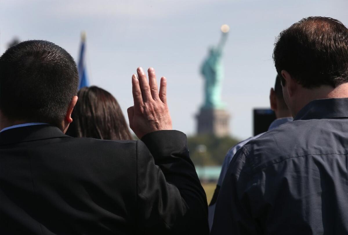Immigrants take the oath of citizenship at a naturalization ceremony last month in New Jersey, with the Statue of Liberty visible in the background.