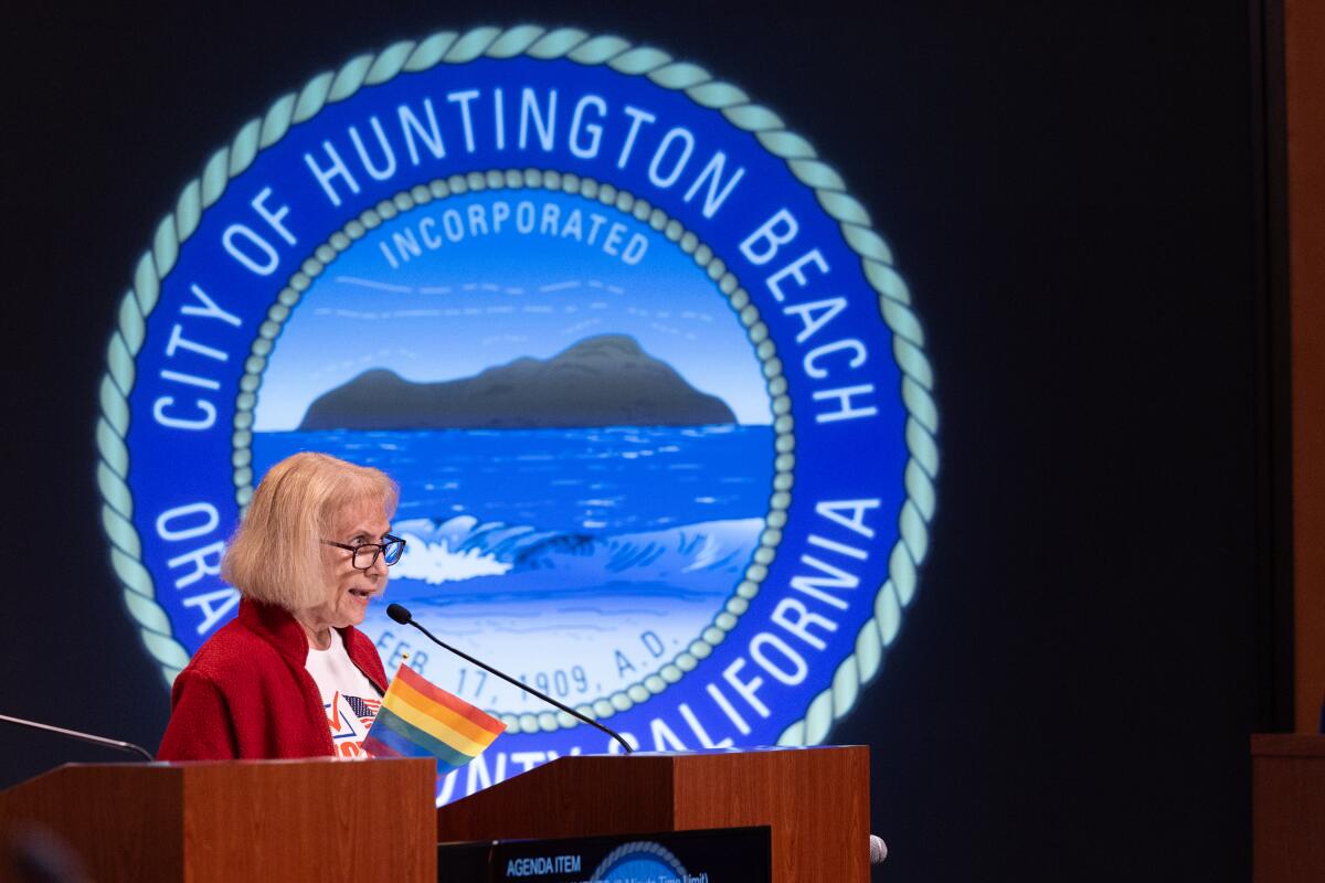 Carol Daus speaks at a lectern in front of the Huntington Beach city seal.