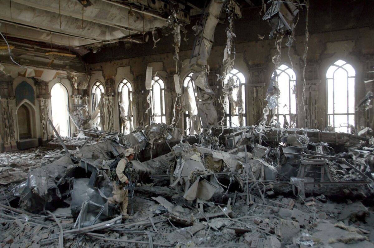A soldier is seen amid masses of rubble inside a building with rows of ornate windows in the background.