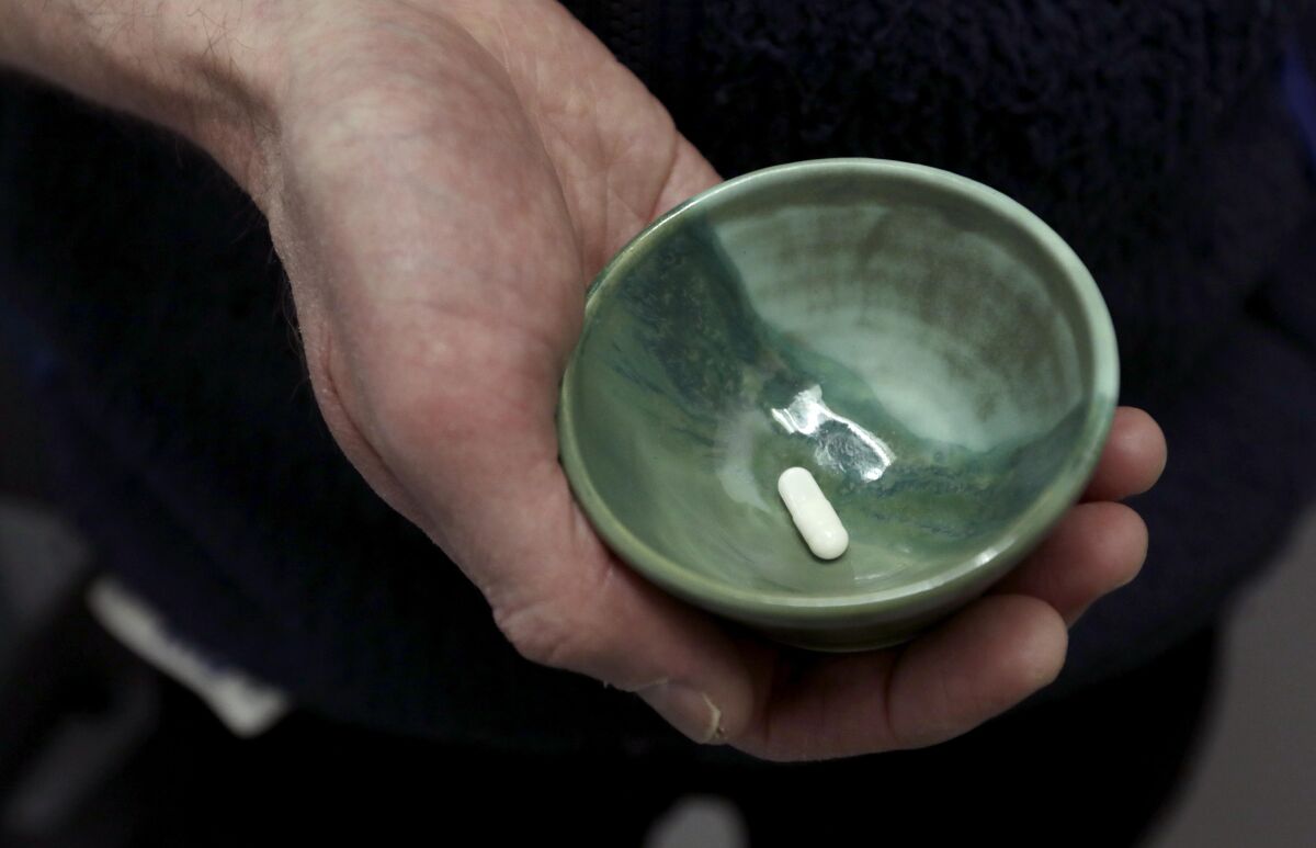 A green bowl containing a white capsule rests in the palm of a hand