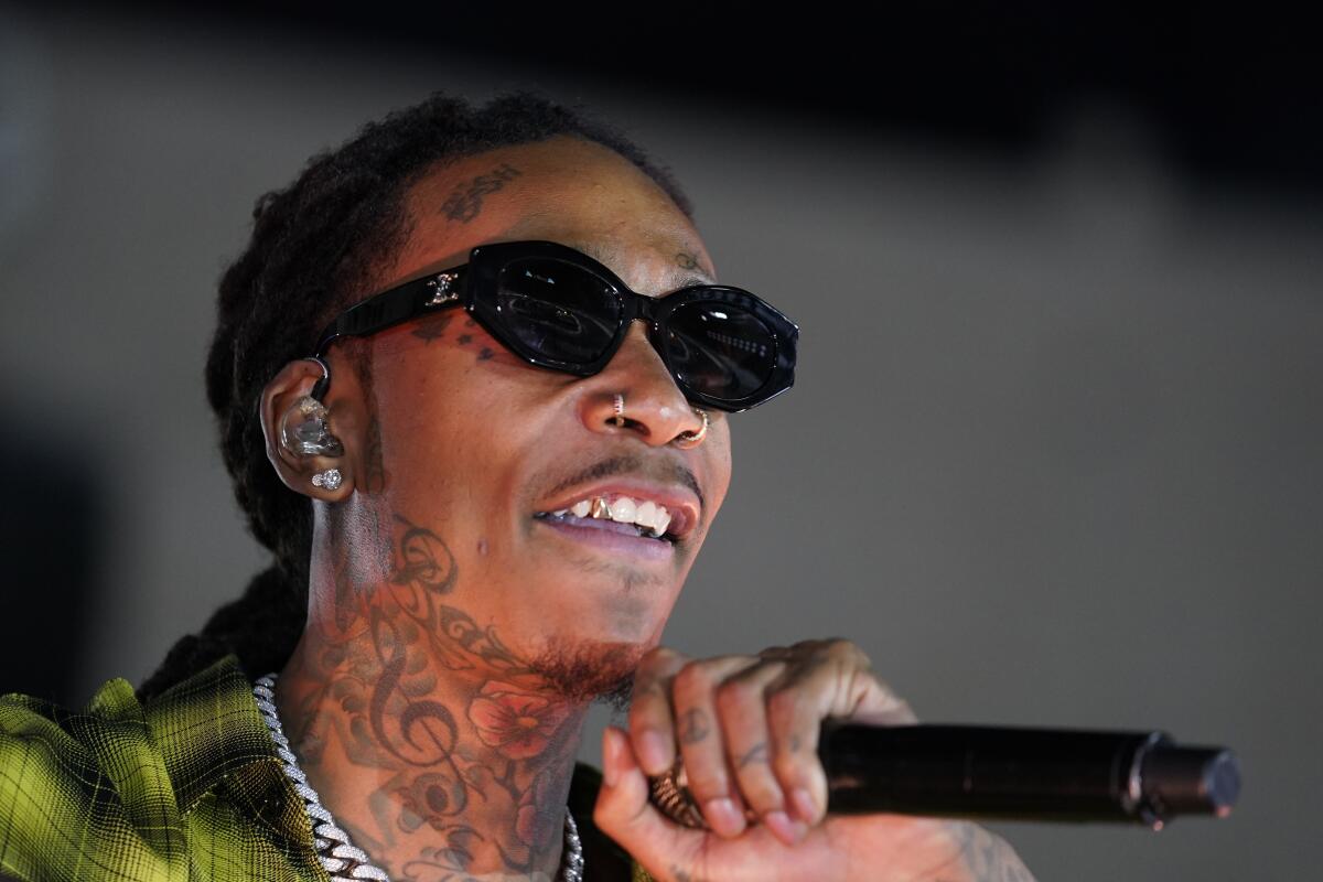 Wiz Khalifa holds a microphone close to his neck while wearing dark sunglasses.