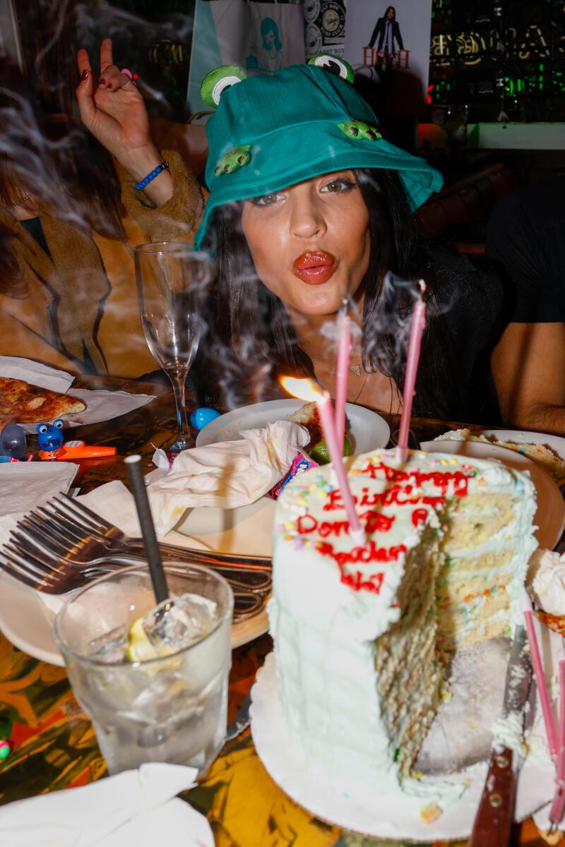 A woman in a green hat blows out candles on a birthday cake