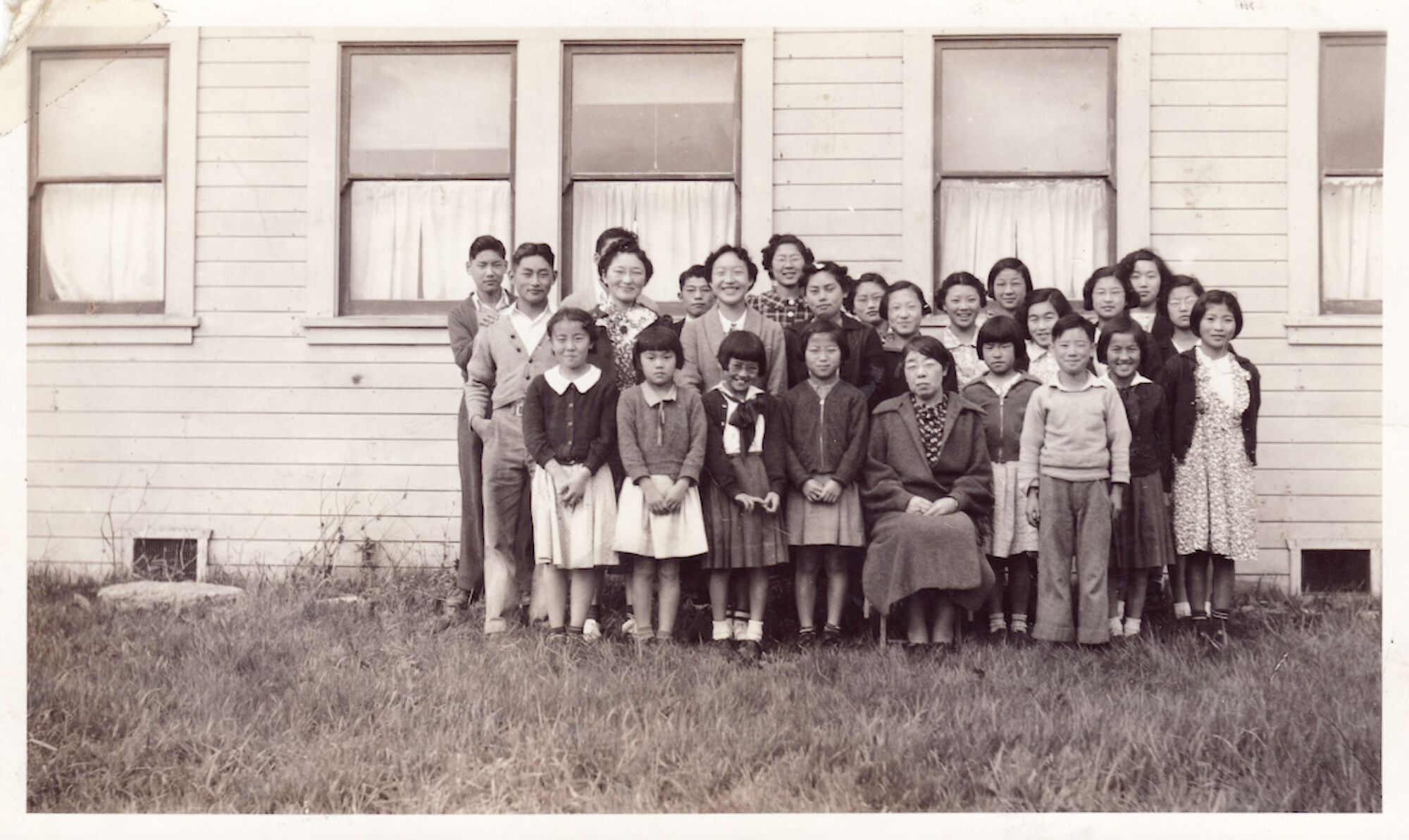 A black-and-white photograph of children and their teacher outside school