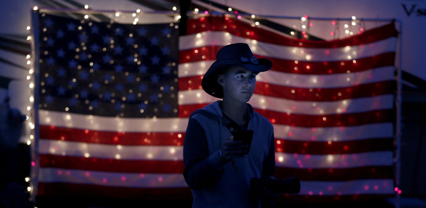 Nick Michael, of Anaheim, checks his phone by an illuminated American flag hanging on an RV at dusk in the RV Resort at the Stagecoach Country Music Festival.
