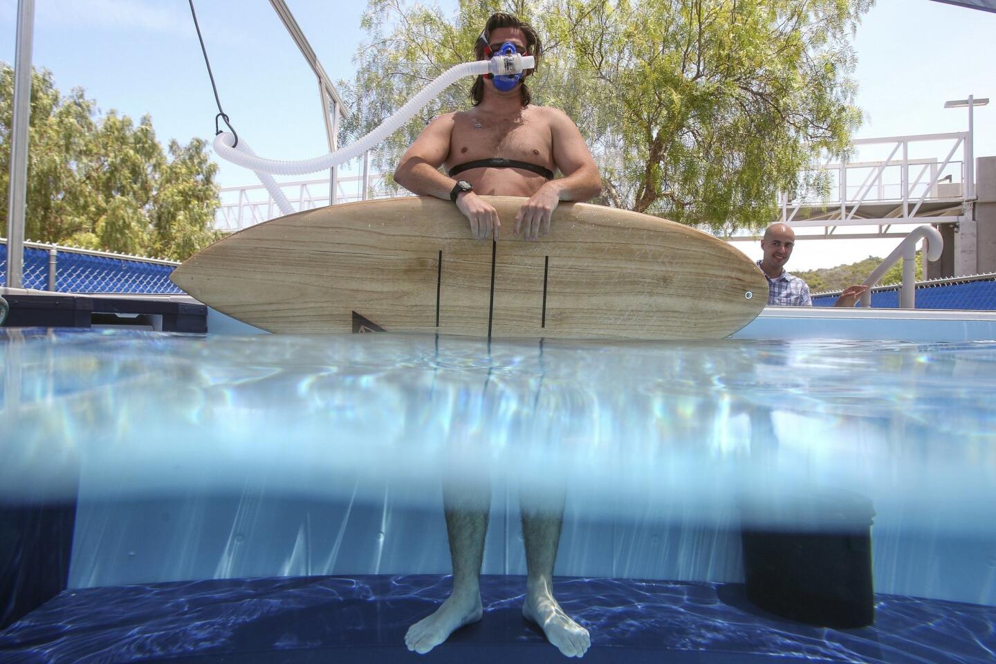 Kinesiology student and intern Cody Cuchna, 24, holds a surfboard while wearing a mask, to measure oxygen consumption, as he gets ready to paddle a surfboard in the swim flume.