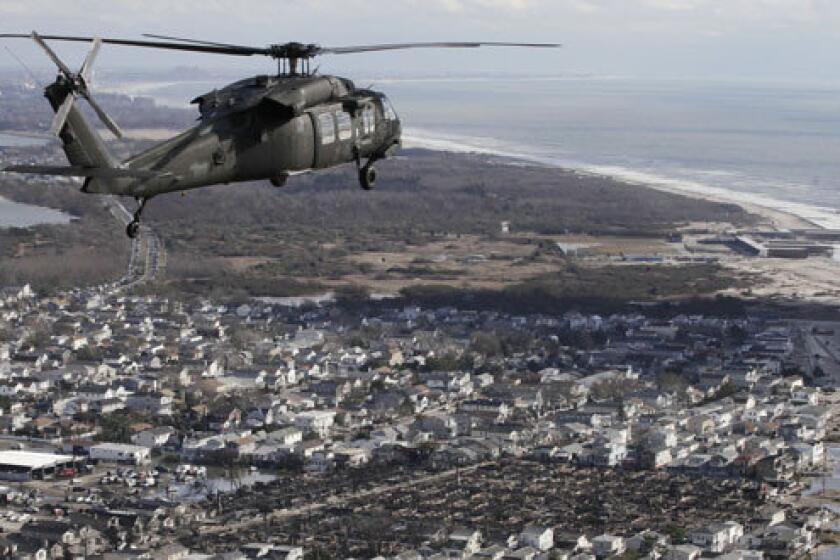 An Air National Guard helicopter flies above the Breezy Point neighborhood in New York where more than 100 homes, lower right, were burned to the ground during superstorm Sandy.