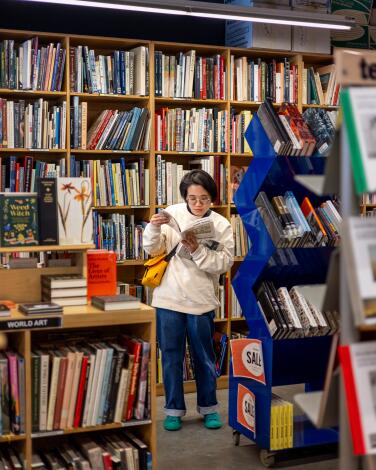 A person stands in front of and among bookshelves, flipping through a book