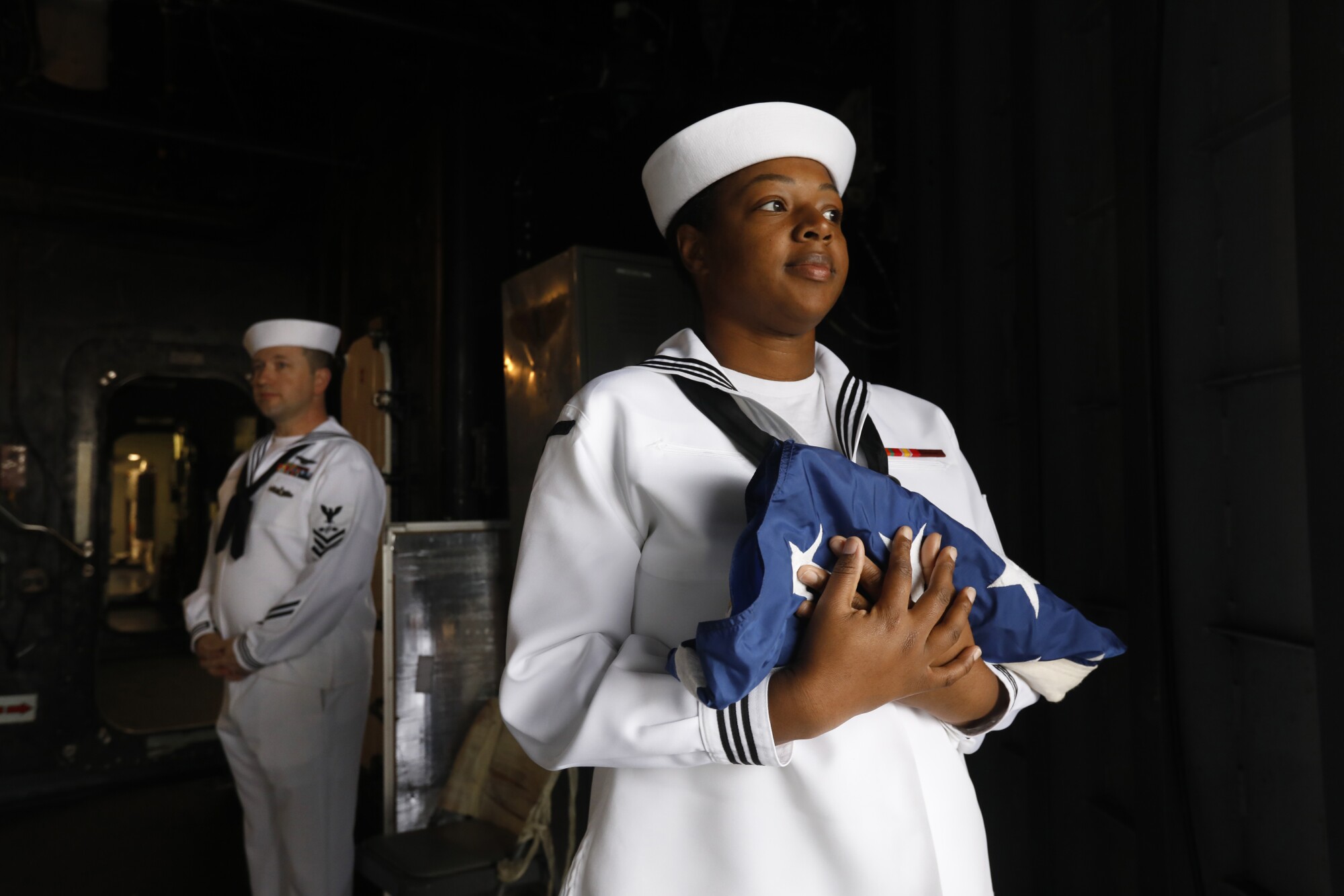 Petty Officer 2nd Class La’Tansia Smith, an operational specialist on the USS Essex, holds a flag before morning colors.