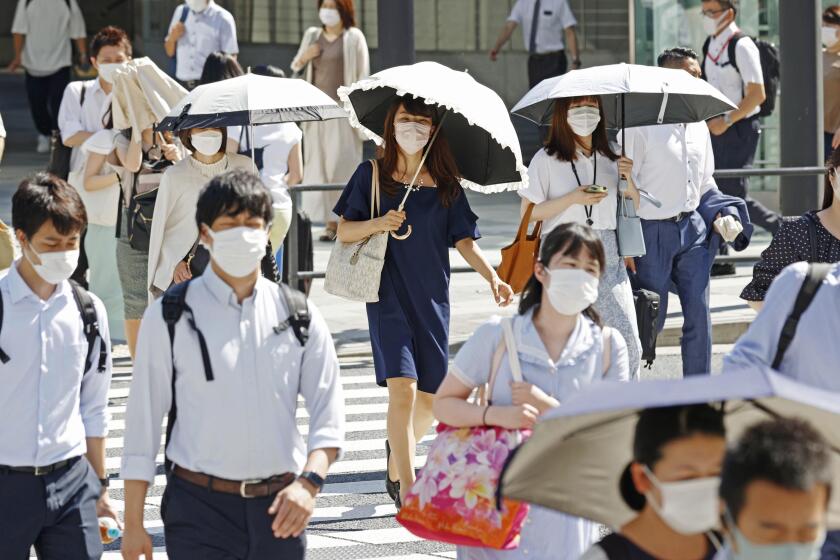 People, some of them holding parasols, cross an intersection amid heat, in Tokyo, Monday, June 27, 2022. Japan’s government issued a warning for possible power crunch in the Tokyo area Monday, asking offices and residents to save energy as the capital region is hit by sweltering heat, with weather officials announcing an earliest end to the rainy season in decades. (Yusuke Ogata/Kyodo News via AP)