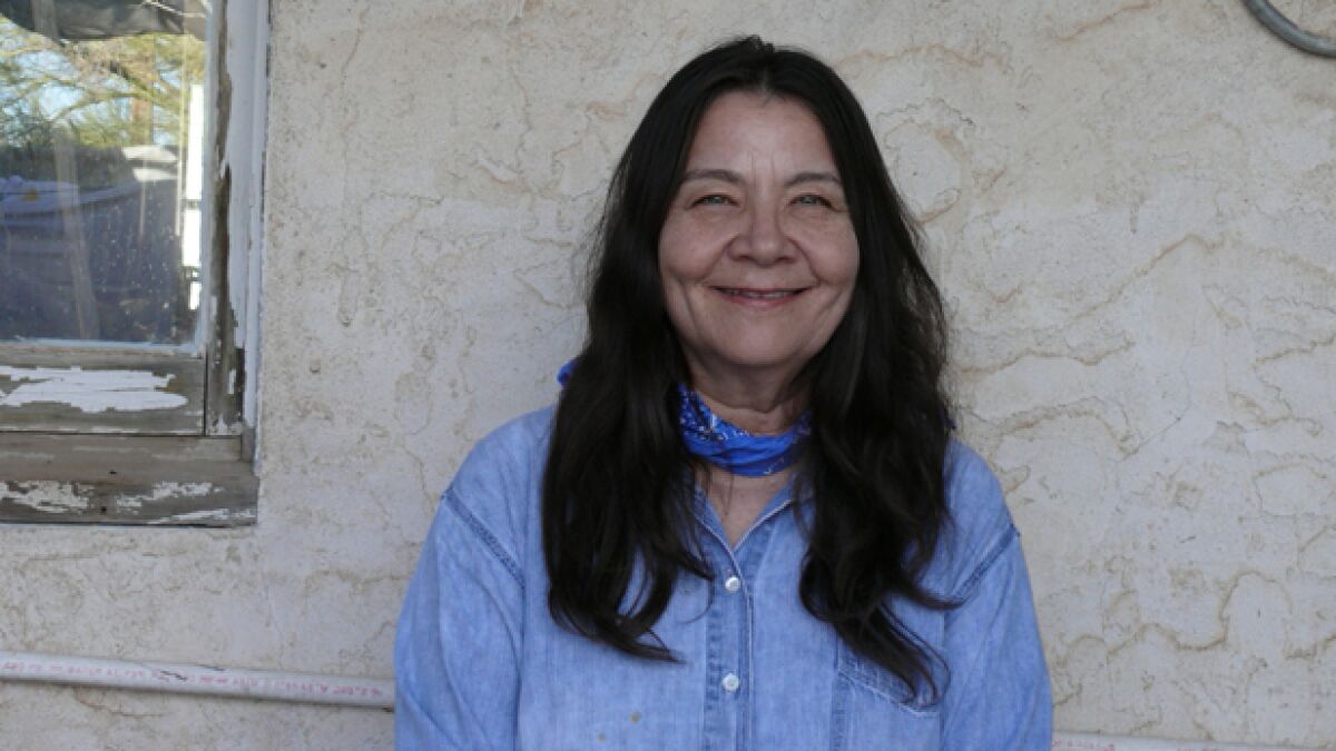  Leslie Marmon Silko stands against a wall and smiles.