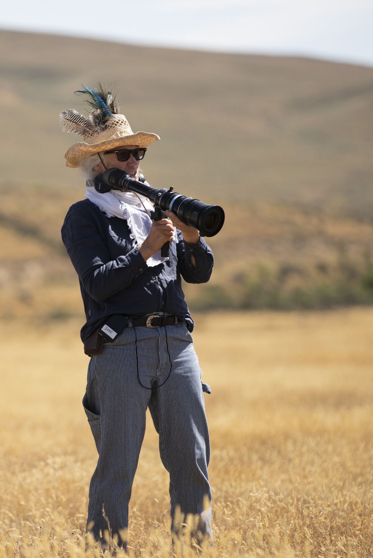 A woman holding a long camera lens stands in a field.