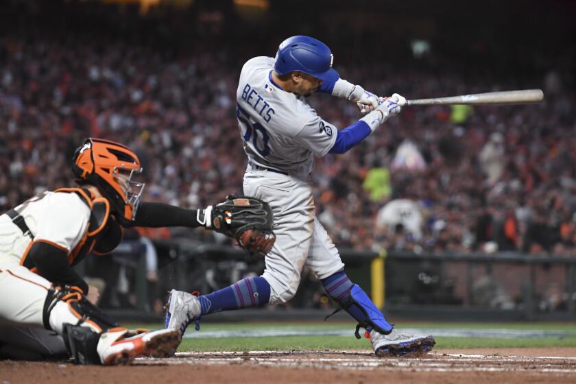 San Francisco, CA - October 09: Los Angeles Dodgers' Mookie Betts follows through on a swing for an RBI single to score AJ Pollock as San Francisco Giants catcher Buster Posey looks on during the second inning of game two in the 2021 National League Division Series at Oracle Park on Saturday, Oct. 9, 2021 in San Francisco, CA. (Wally Skalij / Los Angeles Times)