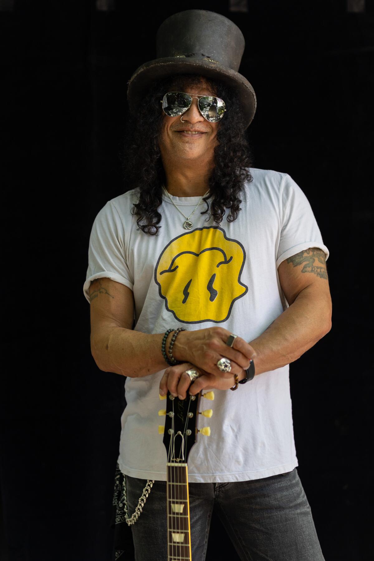 Slash stands, his hands resting on the top of a guitar's headstock