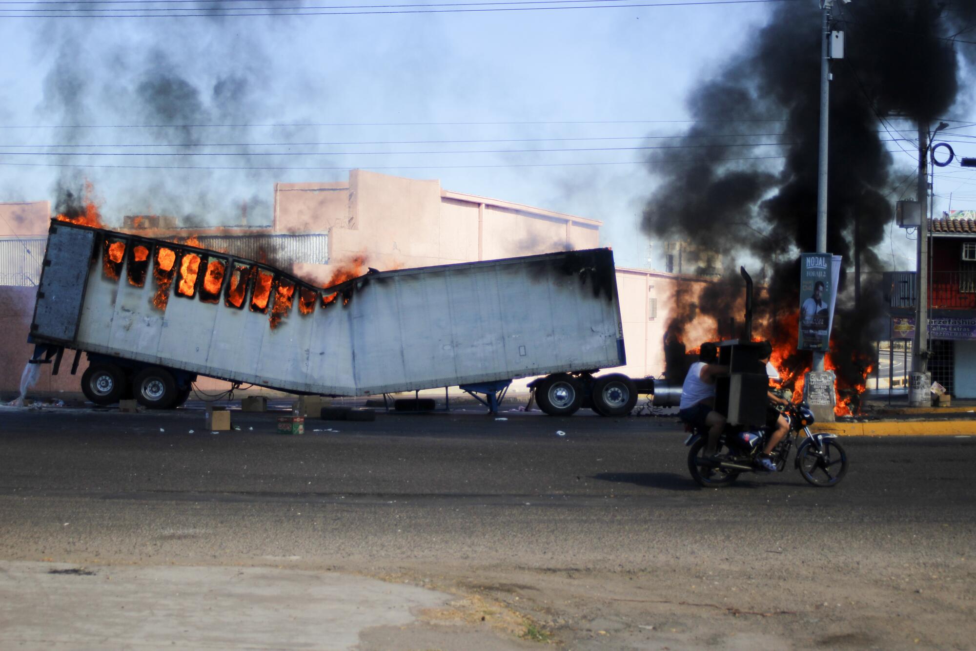 Men ride on a motorcycle past a burning truck on the streets of Culiacán, Sinaloa