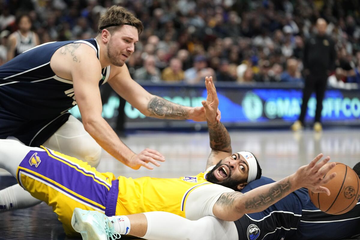 Lakers forward Anthony Davis is sprawled out on the court reaching for a ball while guard Luka Doncic hovers over him 