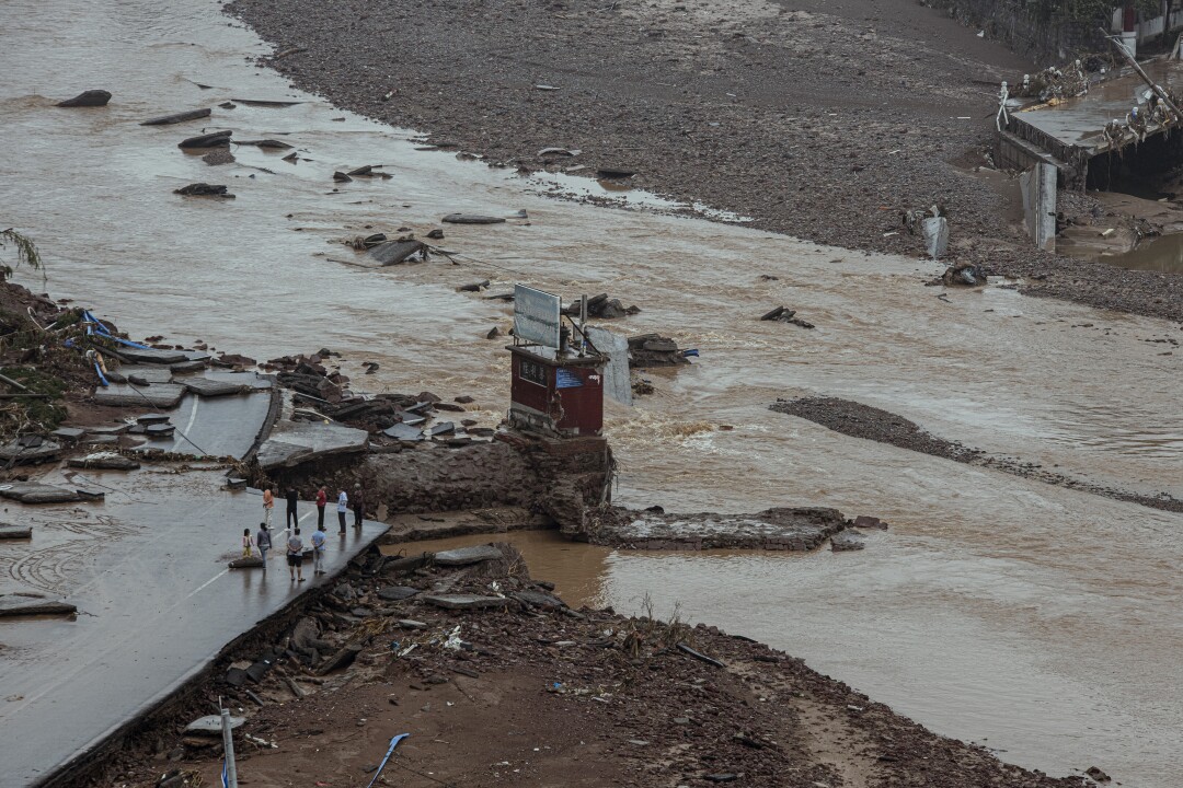 A view of people standing at the edge of a bridge, part of which has been washed away