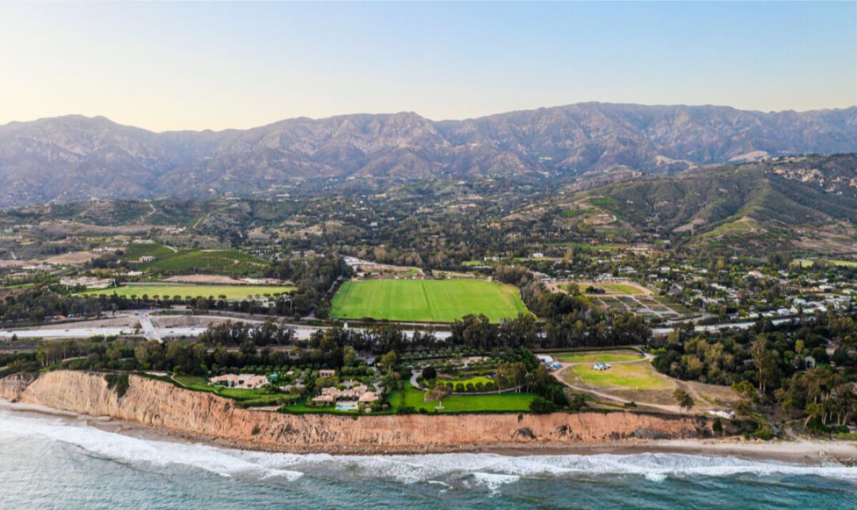 Aerial view of coastal parcels of land backed by mountains, including a large green swath.