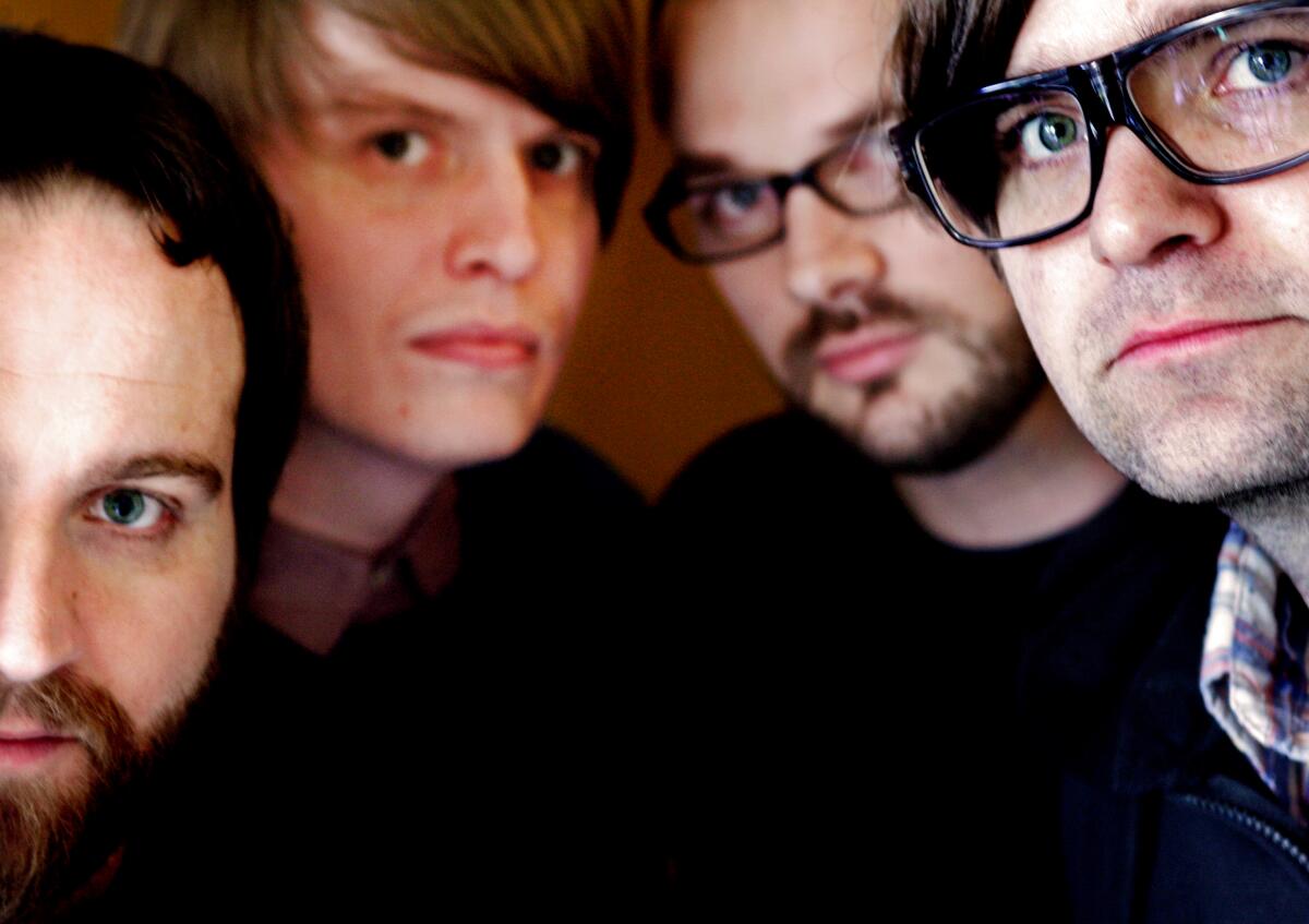 The four members of Death Cab for Cutie look into the camera, their faces partially obscured. 