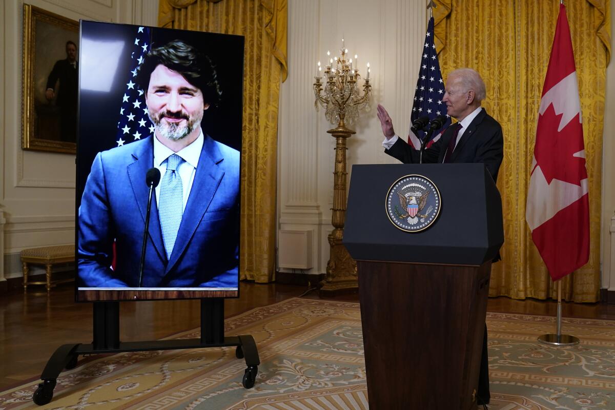 President Biden waves at a screen with Canadian Prime Minister Justin Trudeau on it during a virtual meeting
