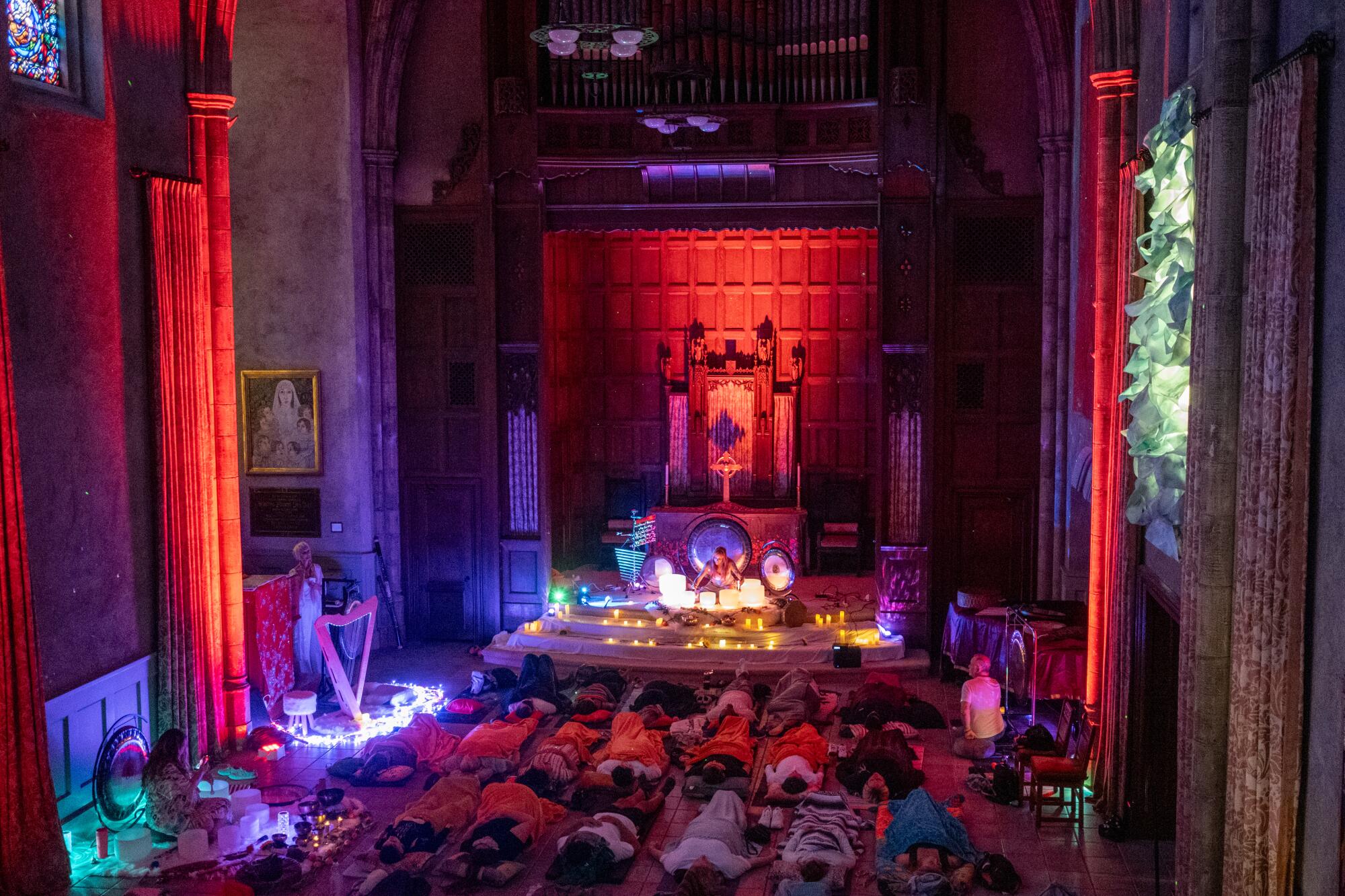 Sound bath guests lay on the floor in a neo-Gothic church. A harp, glowing bowls and uplighting fills the room.